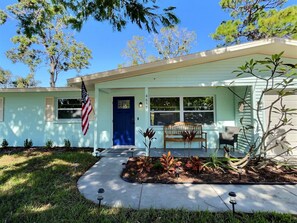 A single-story house with a blue door, a front porch with a bench, and an American flag. - Blue Ranch Retreat (Sarasota)