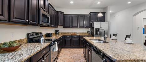 A modern kitchen with dark cabinetry, granite countertops, stainless steel appliances, and a large island with a sink.