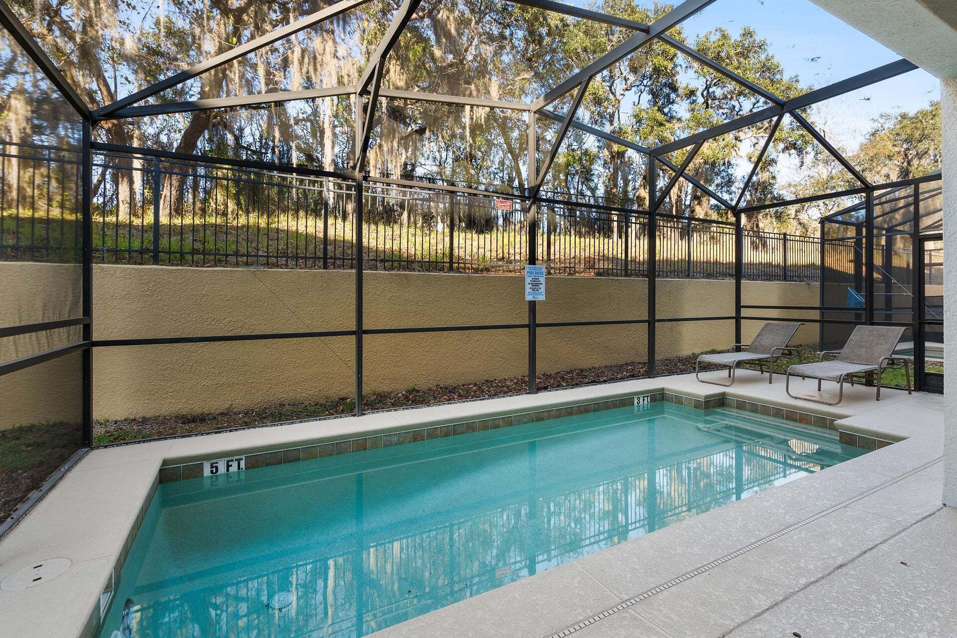 Una piscina con cerramiento de vidrio, rodeada por una cerca metálica y un espacio con bancos.