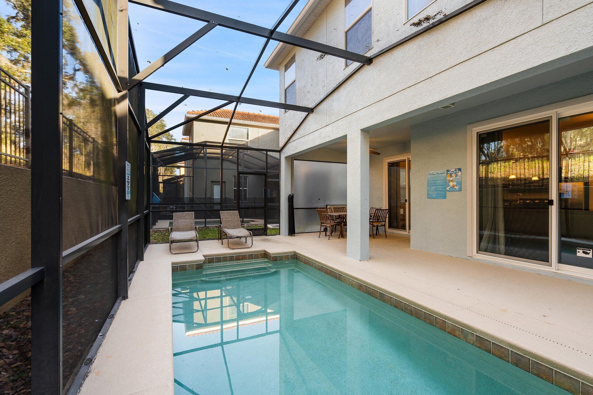 Une piscine entourée de parois en verre, un espace extérieur aménagé avec des sièges et un patio couvert.