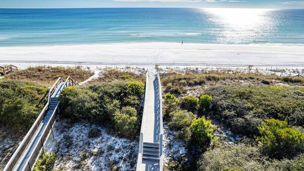 A beach with a wooden boardwalk leading to the water, surrounded by vegetation. - Little Wing (Santa Rosa Beach)