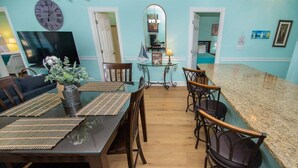 A dining area with a wooden table, chairs, a vase with flowers, a clock, and a mirror on the wall. - Magnolia Place 4789-103 (Myrtle Beach)