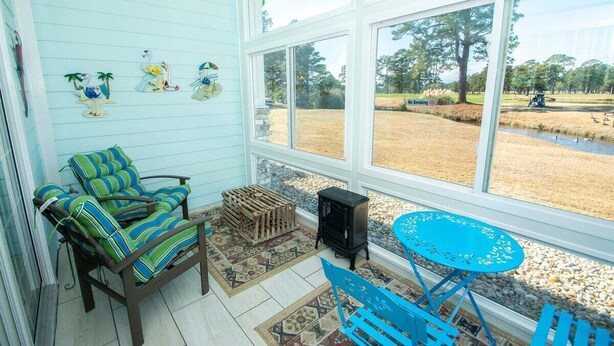A sunroom with a view of a golf course, a wooden table, and striped chairs. - Magnolia Place 4789-103 (Myrtle Beach)