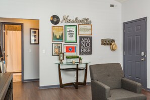 A room with a glass-top table, a grey armchair, and wall-mounted decorations including framed pictures and a vinyl record. - Looby Location- Charming 3br Home 10 min to Downtown! (Nashville)