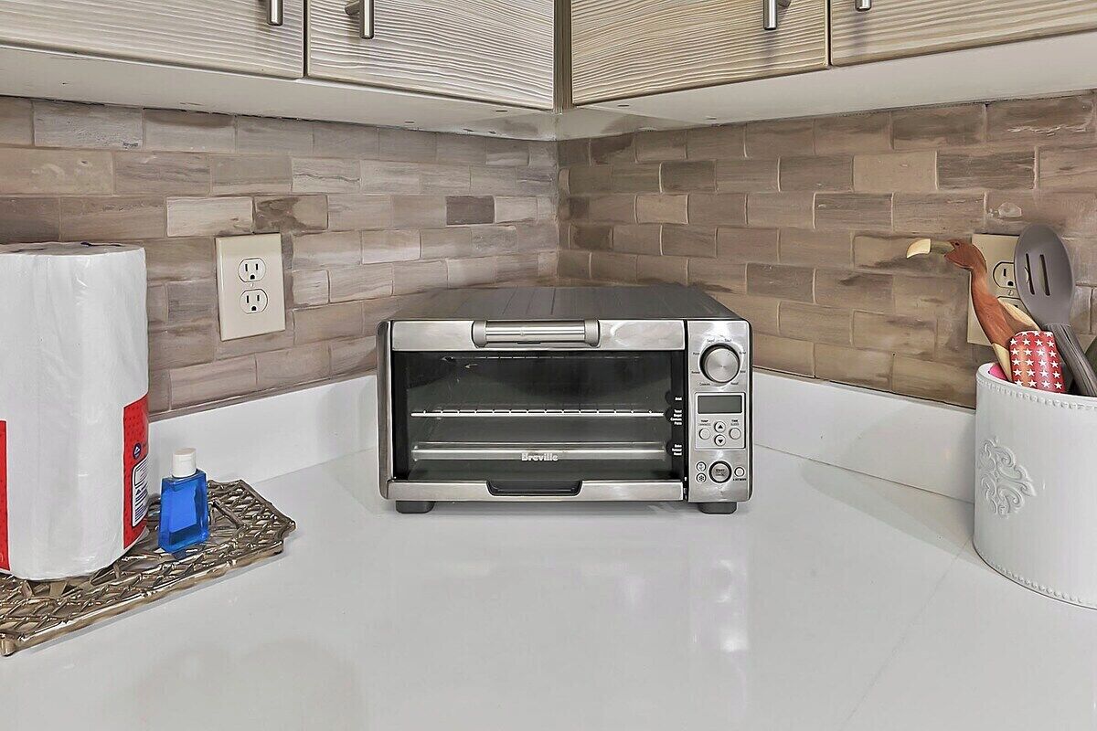 A kitchen with a built-in toaster oven, a white countertop, and a backsplash with wooden tiles.