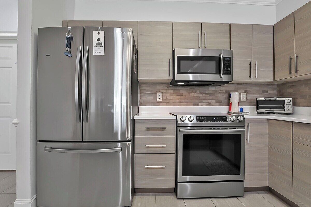 Uma cozinha moderna com eletrodomésticos de aço inoxidável, incluindo geladeira, micro-ondas, forno e torradeira.