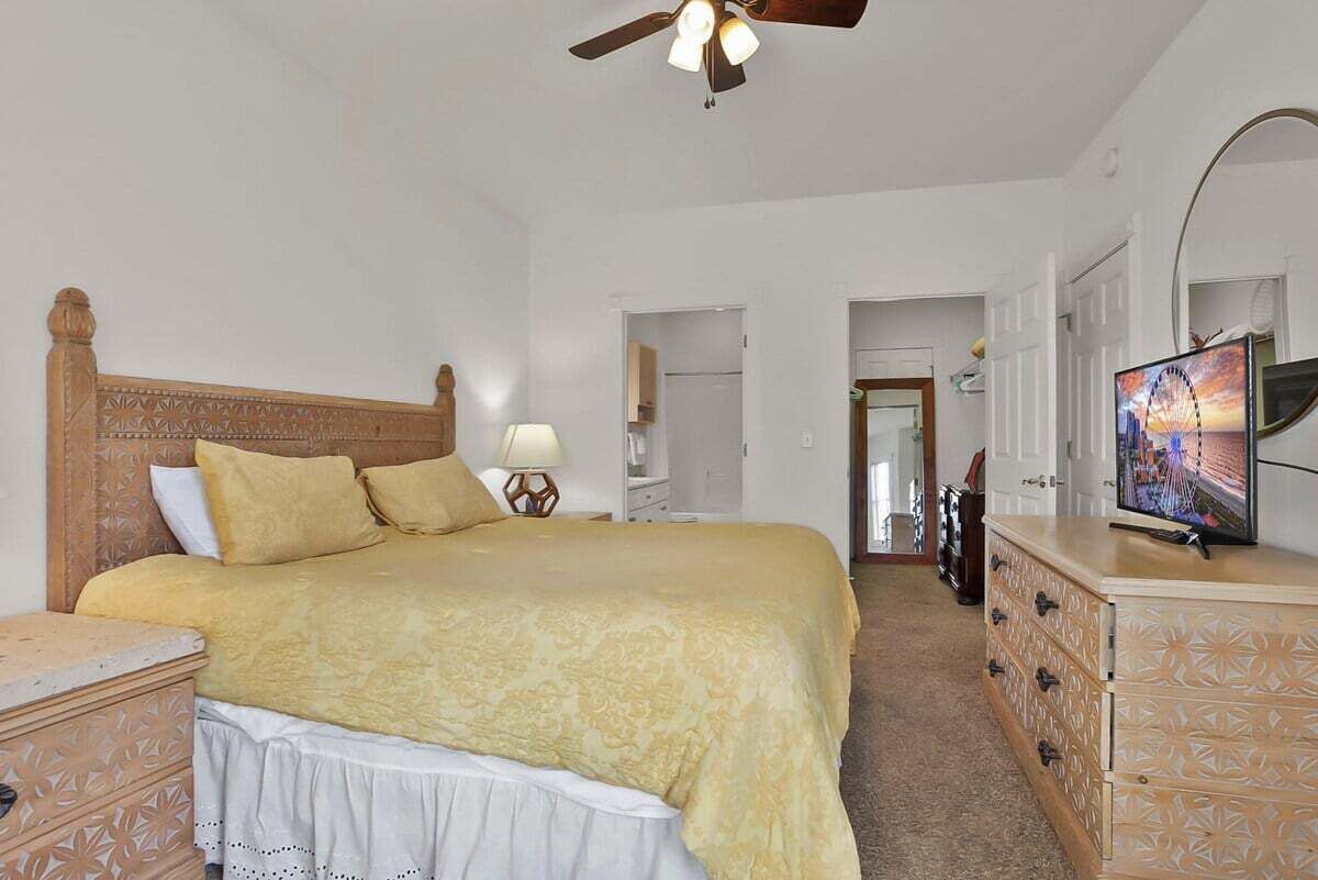 A bedroom with a bed, a ceiling fan, a dresser, and a television.