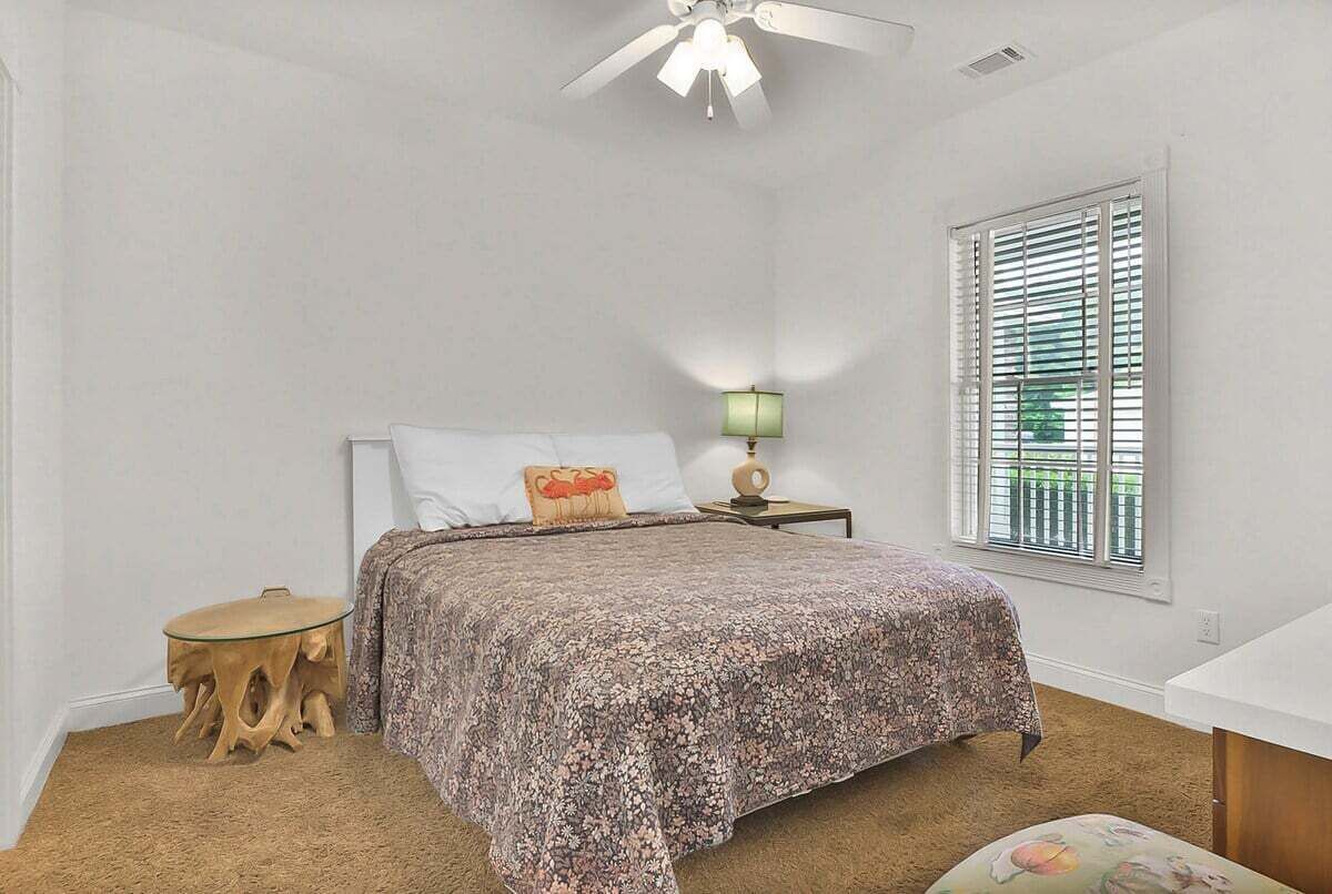 Um quarto com uma cama, uma mesa de cabeceira, um abajur, uma janela com persianas e uma pequena mesa redonda.