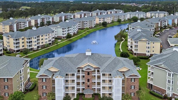 A residential complex with multiple apartment buildings, a central water feature, and a well-maintained lawn. - Magnolia Pointe Luster Leaf 4825-102 (Myrtle Beach)