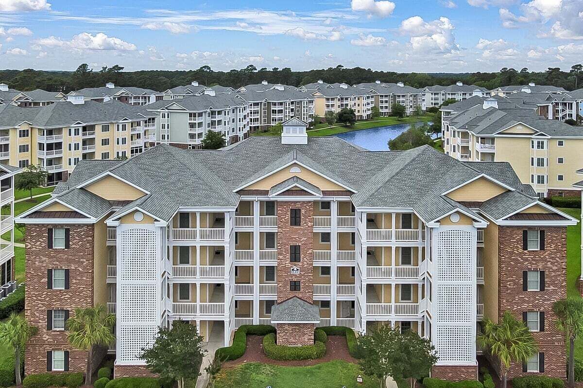 A multi-story hotel with a central courtyard, balconies, and a swimming pool in the background.