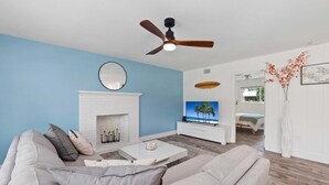 Ein modernes Wohnzimmer mit weißem Kamin, Deckenventilator, Flachbildfernseher und einer Couch.