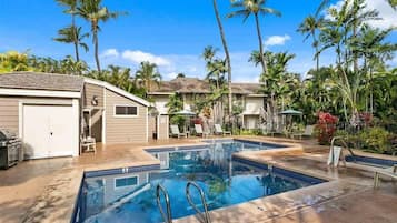 A swimming pool with two diving boards, surrounded by palm trees and a covered patio area.