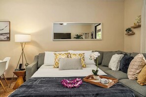 A hotel room with a bed, a bedside table with a lamp, a mirror, a sofa, and a small plant. - Wailea Luxury Retreat Walk to Beach & Shops (Kihei)