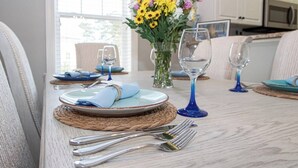 Una mesa de comedor dispuesta con platos, cubiertos y copas de vino, con un jarrón de flores al fondo.