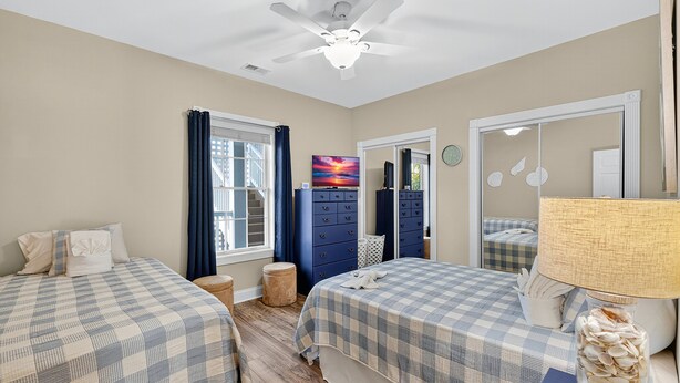 Une chambre avec deux lits, un ventilateur de plafond, une commode et une fenêtre avec des rideaux.