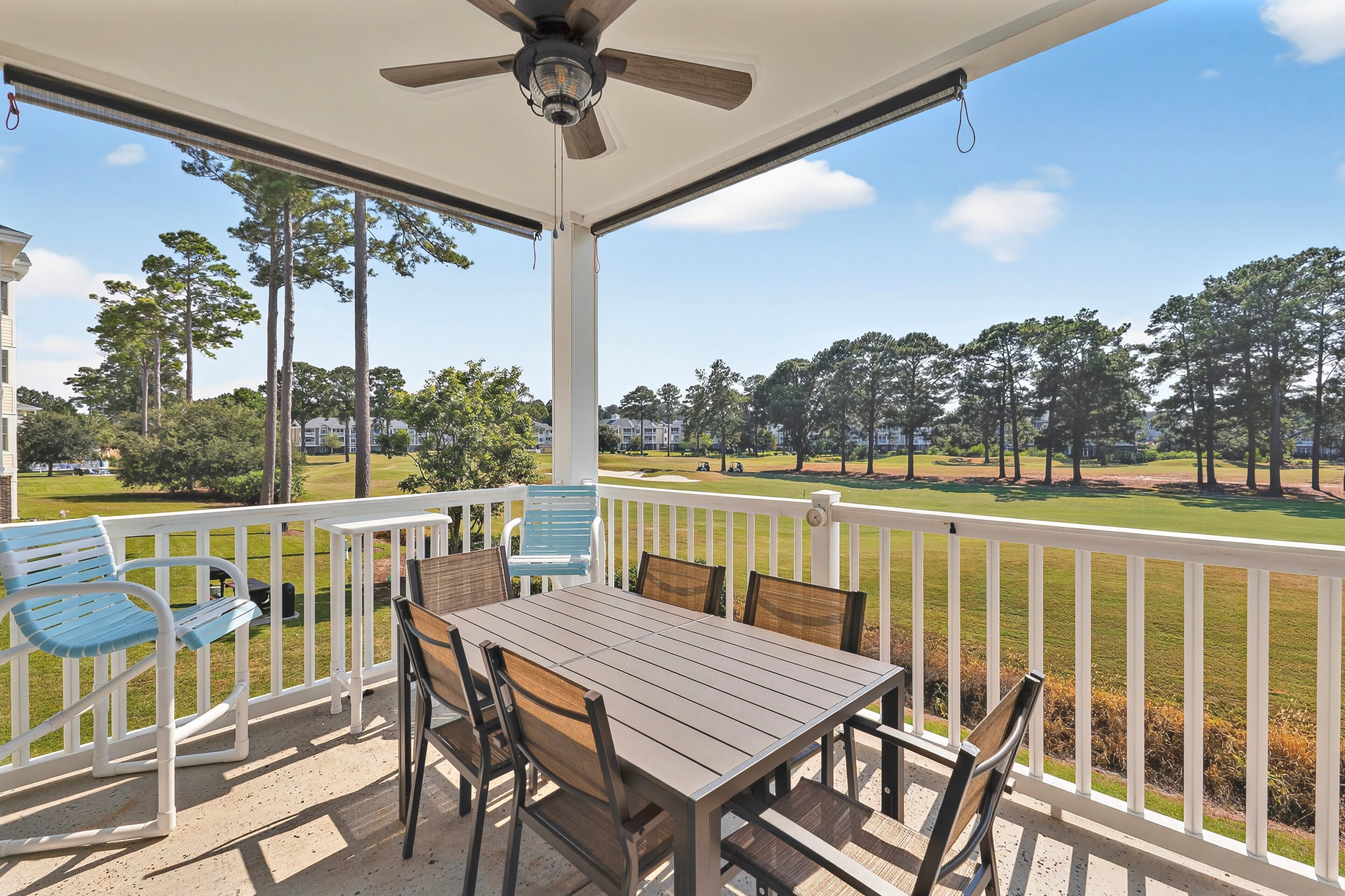 A covered patio with a table and chairs, overlooking a golf course.
