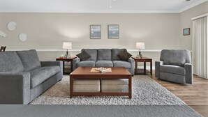 Un salon avec un canapé gris, un fauteuil assorti, une table basse en bois et deux petites tables d’appoint avec des lampes.
