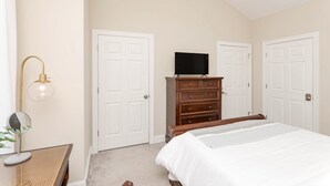 Een slaapkamer met een bed, een dressoir, een televisie en een lamp.