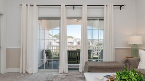 Een woonkamer met een grote schuifpui die uitkomt op een balkon, een groene stoel, een bruine bank, een witte salontafel en een lamp.