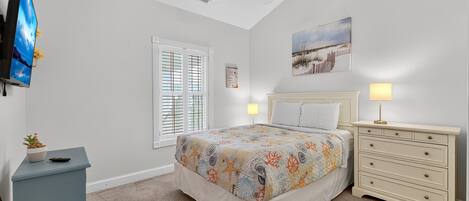 A bedroom with a bed, bedside tables, a ceiling fan, a window with blinds, and a wall-mounted TV.