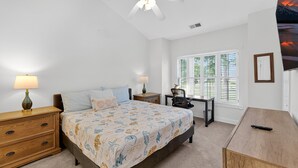 Une chambre à coucher comprenant un lit, des tables de chevet, un bureau et un ventilateur de plafond.