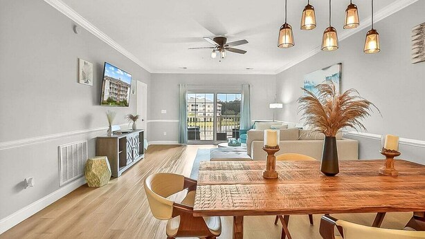 A dining area with a wooden table, chairs, and hanging pendant lights. - Magnolia Pointe Magnolia Lake 4820-303 (Myrtle Beach)