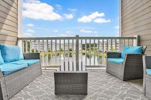 A balcony with wicker furniture and a view of a building across a body of water. - Magnolia Pointe Magnolia Lake 4820-303 (Myrtle Beach)