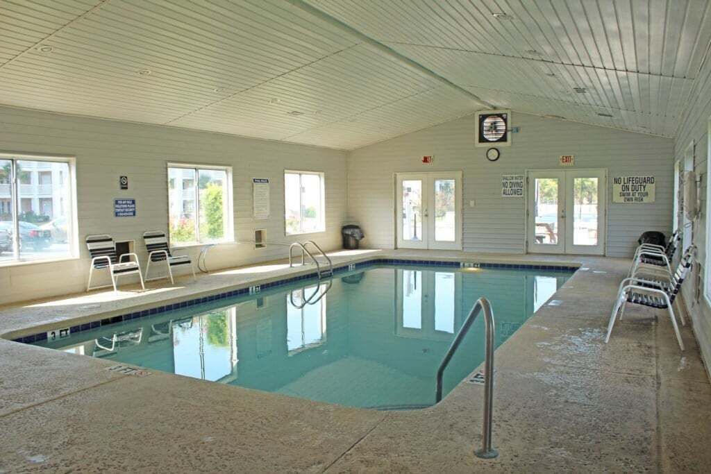 An indoor swimming pool with clear water, a ladder, and a few lounge chairs.