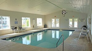 Una piscina interior con agua cristalina, una escalera y algunas sillas reclinables.