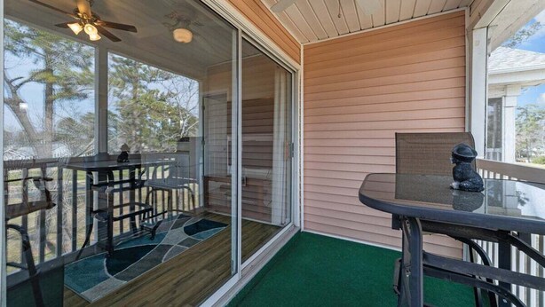 Un patio cubierto con una puerta de cristal que da a una terraza, una mesa con sillas y un ventilador de techo.