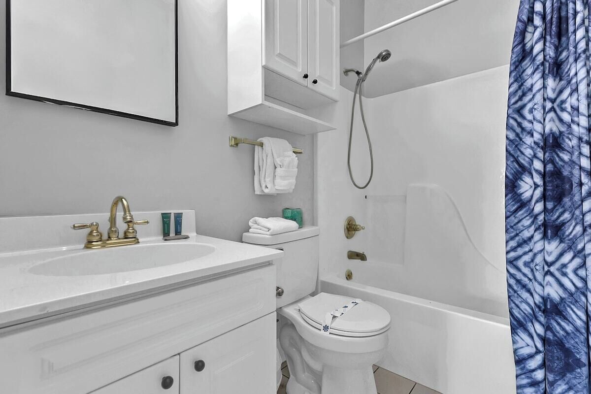 A modern bathroom with a white sink, gold faucet, white toilet, and a shower with a blue patterned curtain.