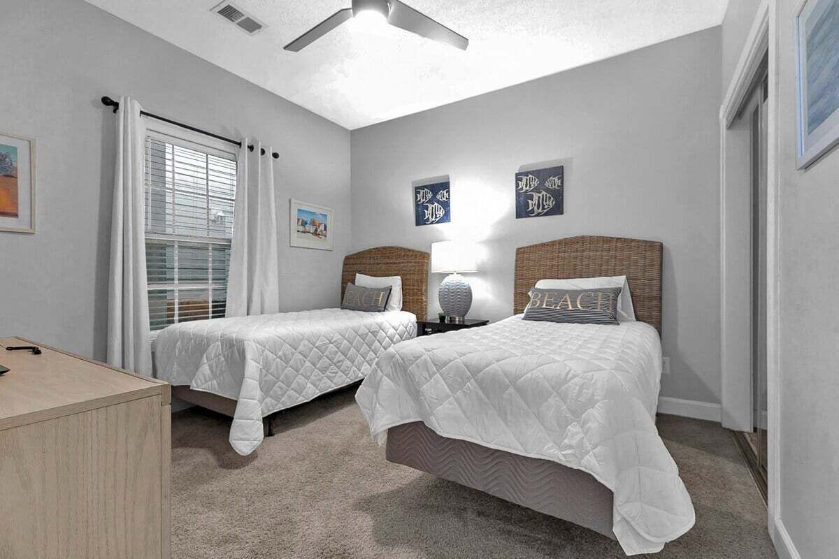 A bedroom with two beds, a desk, and a ceiling fan.