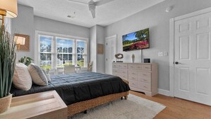 Een slaapkamer met een bed, een dressoir, een plafondventilator, een raam en een deur.