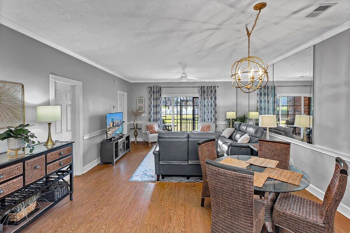 A modern living room with a sofa, dining table, and chairs, a TV, and a large window with curtains.