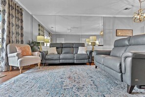 En stue med en grå sofa, en stribet lænestol og et mønstret tæppe.