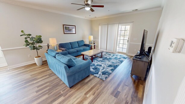 A living room with a sectional sofa, a coffee table, a TV, and a ceiling fan. - Magnolia Pointe 4869-201 (Myrtle Beach)