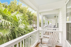 Un portico bianco con una sedia di legno, immerso in un verdeggiante fogliame.