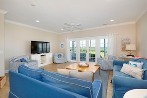 A living room with blue sofas, a television, and a view through glass doors. - Waterfront Luxury Villa With Sunset Views and Boat Slip (Marathon)