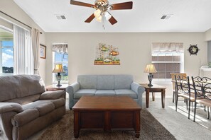 A living room with a sofa, a coffee table, a dining table with chairs, a ceiling fan, and a window with curtains. - Waterway Village 16I (Myrtle Beach)