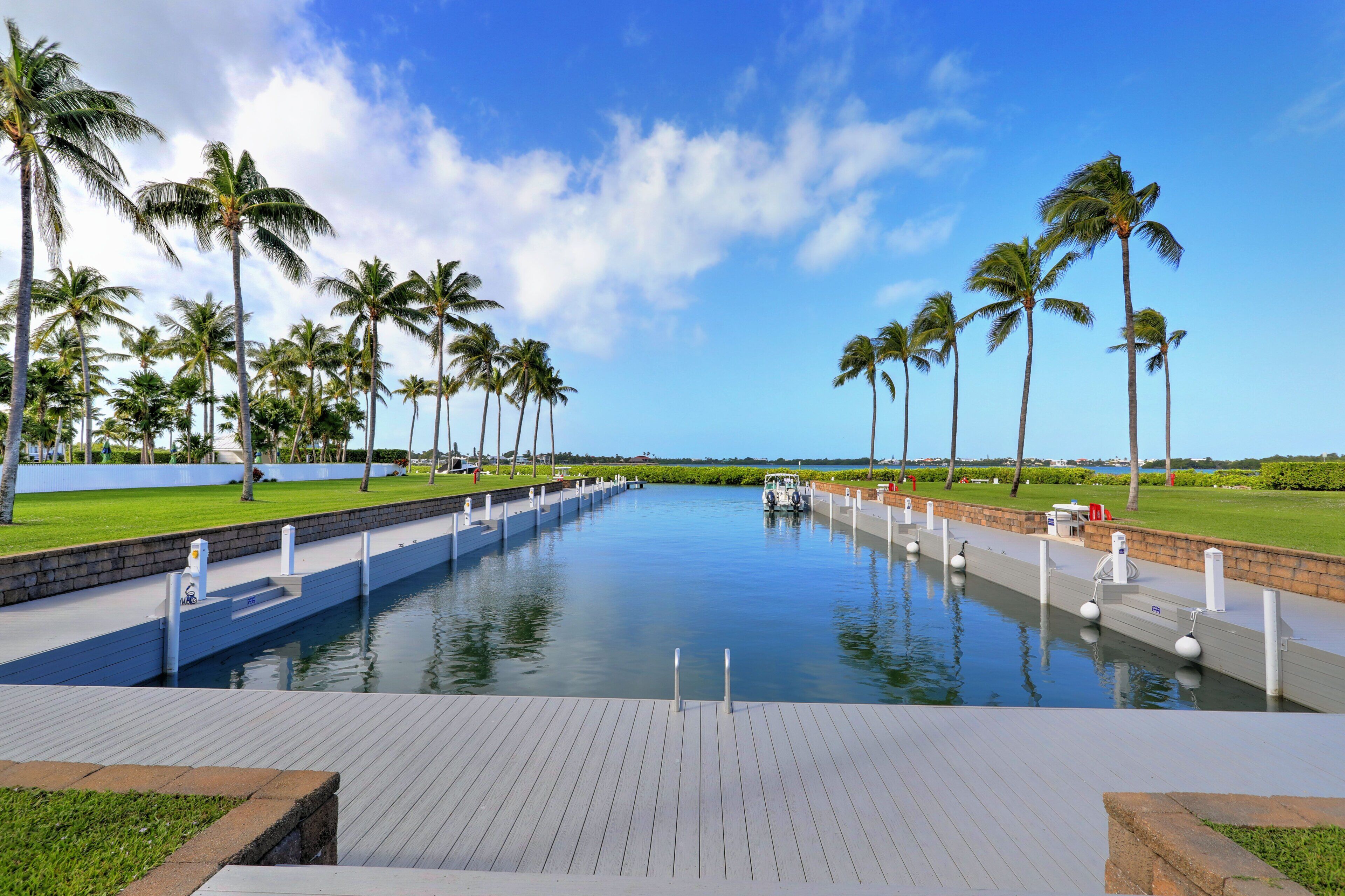 A long, narrow waterway with a wooden deck, surrounded by palm trees and a clear sky.