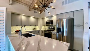 A modern kitchen with a large island, stainless steel appliances, and a unique ceiling light fixture. - Modern Life (Rancho Mirage)