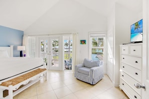 A bedroom with a bed, a nightstand, a dresser, a window with a view, and a door leading to a balcony. - Waterfront Luxury Villa With Sunset Views and Boat Slip (Marathon)