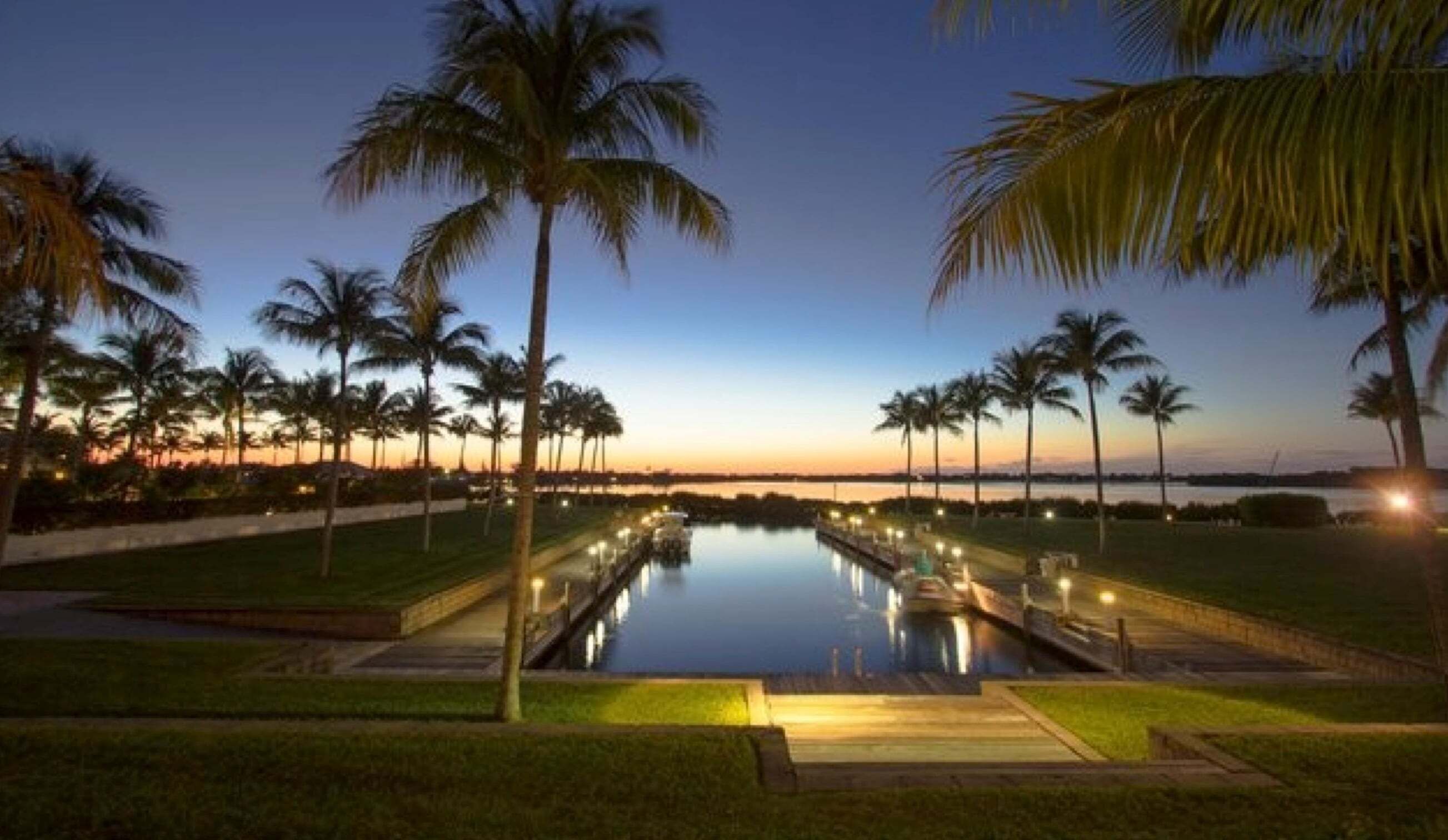A pool with a boat, surrounded by palm trees and a sunset view.