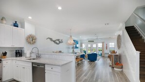 A modern kitchen with white cabinetry, a central island, and a dining area with blue chairs. - Waterfront Luxury Villa With Sunset Views and Boat Slip (Marathon)