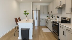 A modern kitchen with stainless steel appliances, wooden flooring, and white cabinetry. - Modern,a+location,workerfriendly,pool,gym,kingbed (Sherman)
