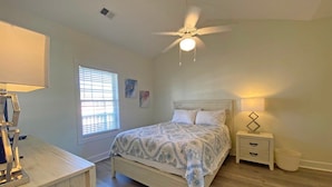 Un dormitorio con cama, mesitas de noche, ventilador de techo y ventana con persianas.