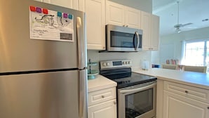 Una cocina con gabinetes blancos, electrodomésticos de acero inoxidable, microondas, horno y refrigerador.