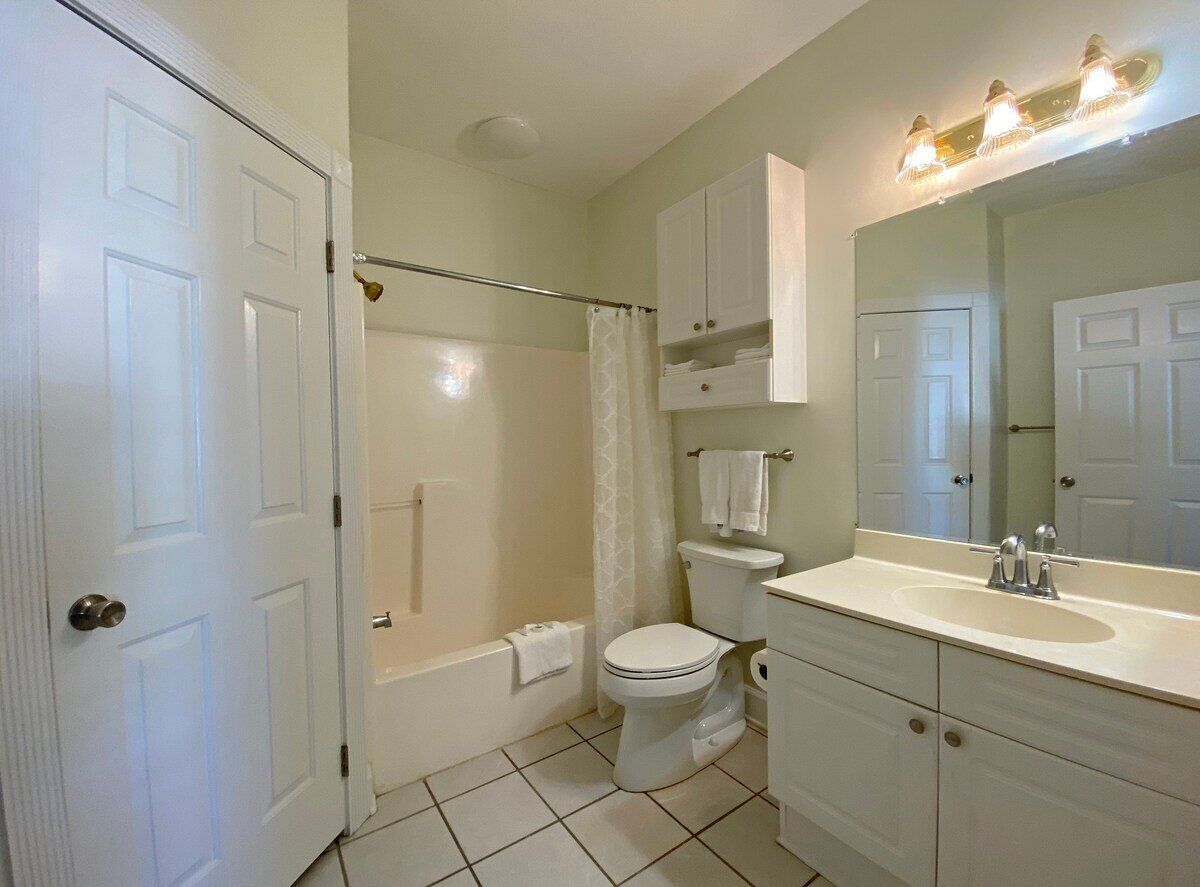 A bathroom with a toilet, sink, mirror, and shower.