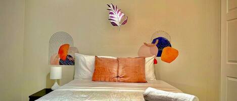 A neatly made bed with a red blanket, white pillows, and a decorative feather on the wall.