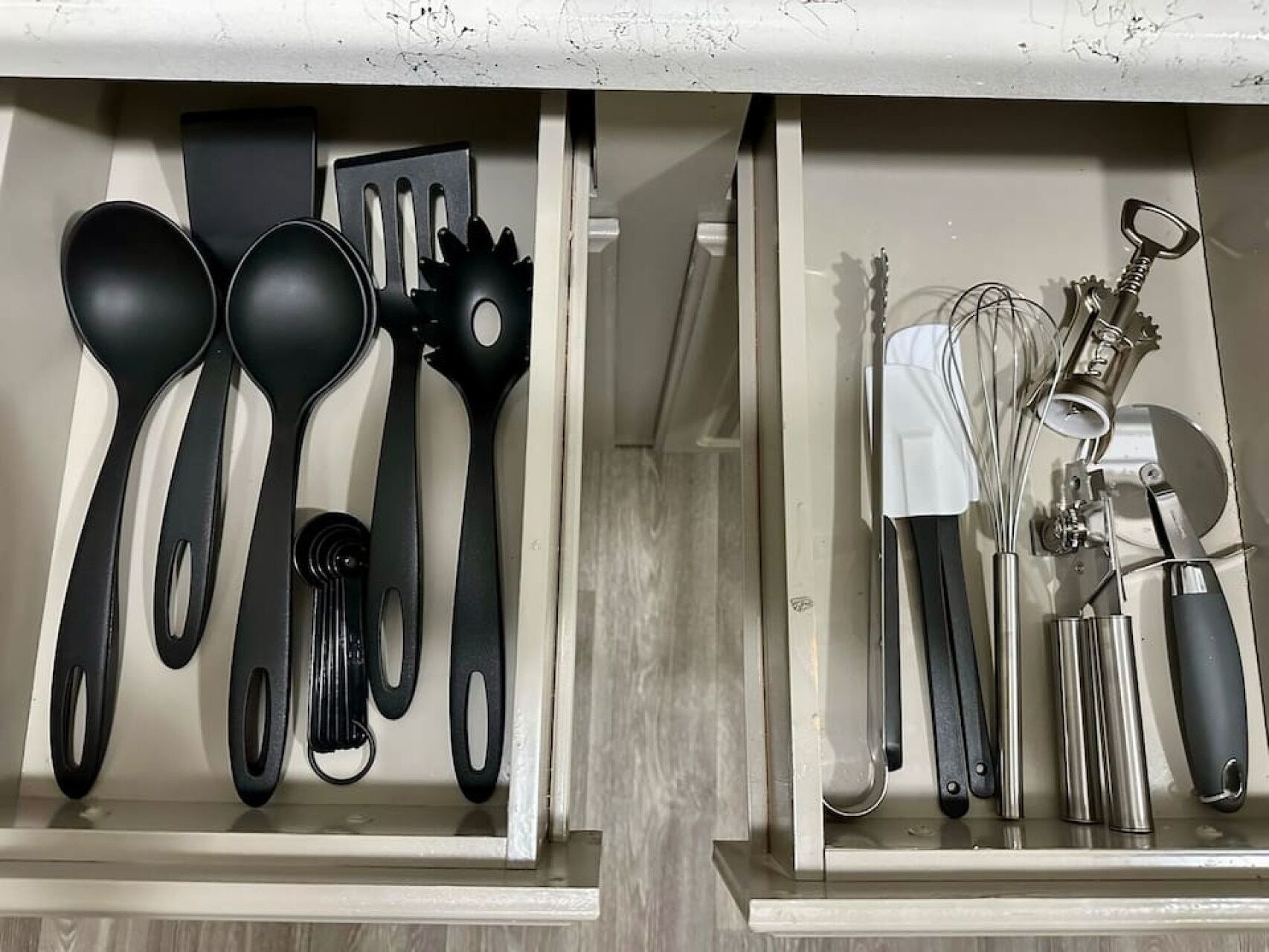A kitchen drawer with black and white utensils, including spoons, spatulas, and a whisk set.